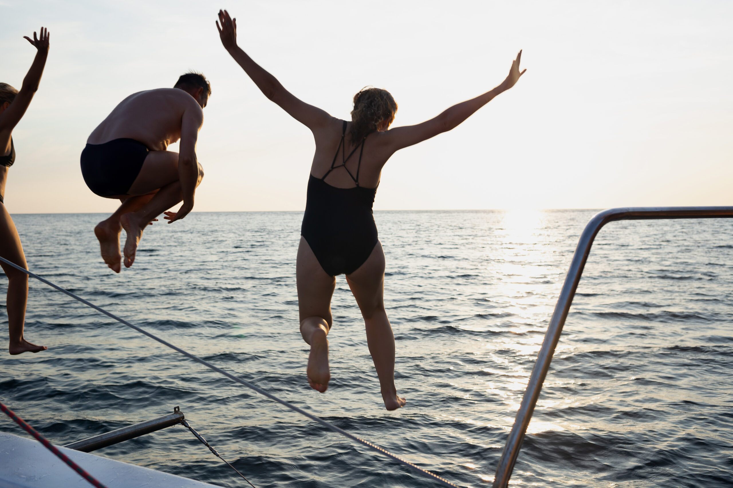 a group of friends jumping into the sea from a yacht at sunset.